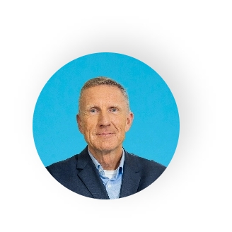 Das Bild zeigt Wolfgang Ehrensperger, einen reiferen Mann, vor einer blauen Wand.