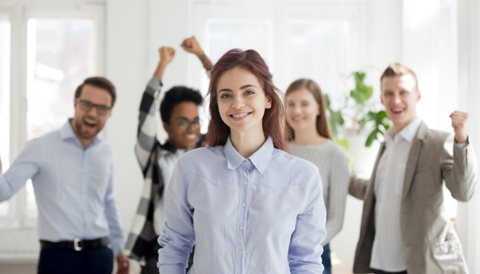 Porträt einer erfolgreichen weibliche Angestellten mit aufgeregten Kollegen im Hintergrund